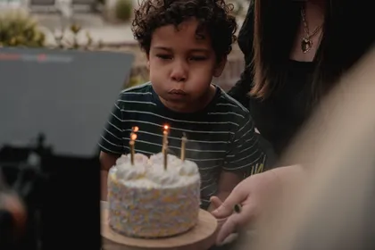 A boy blows out his birthday candles, family gathered around