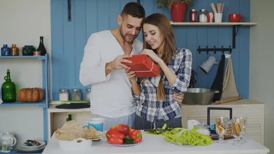 A couple opens a red gift together in their kitchen