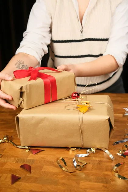 Hands wrapping kraft-paper gifts with red ribbon