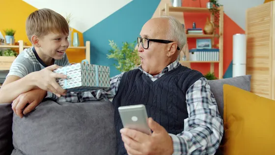 A grandson gives a gift to his delighted, surprised grandfather, phone in hand