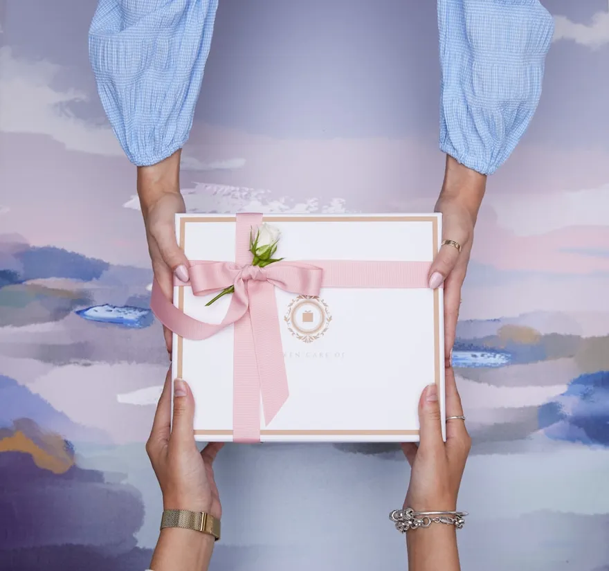 Two hands exchanging a ribboned gift over a painted lilac background
