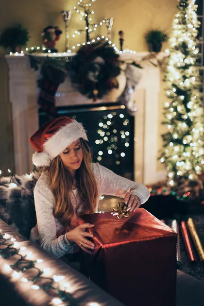 Someone tying a ribbon on a red gift box near a lit Christmas tree